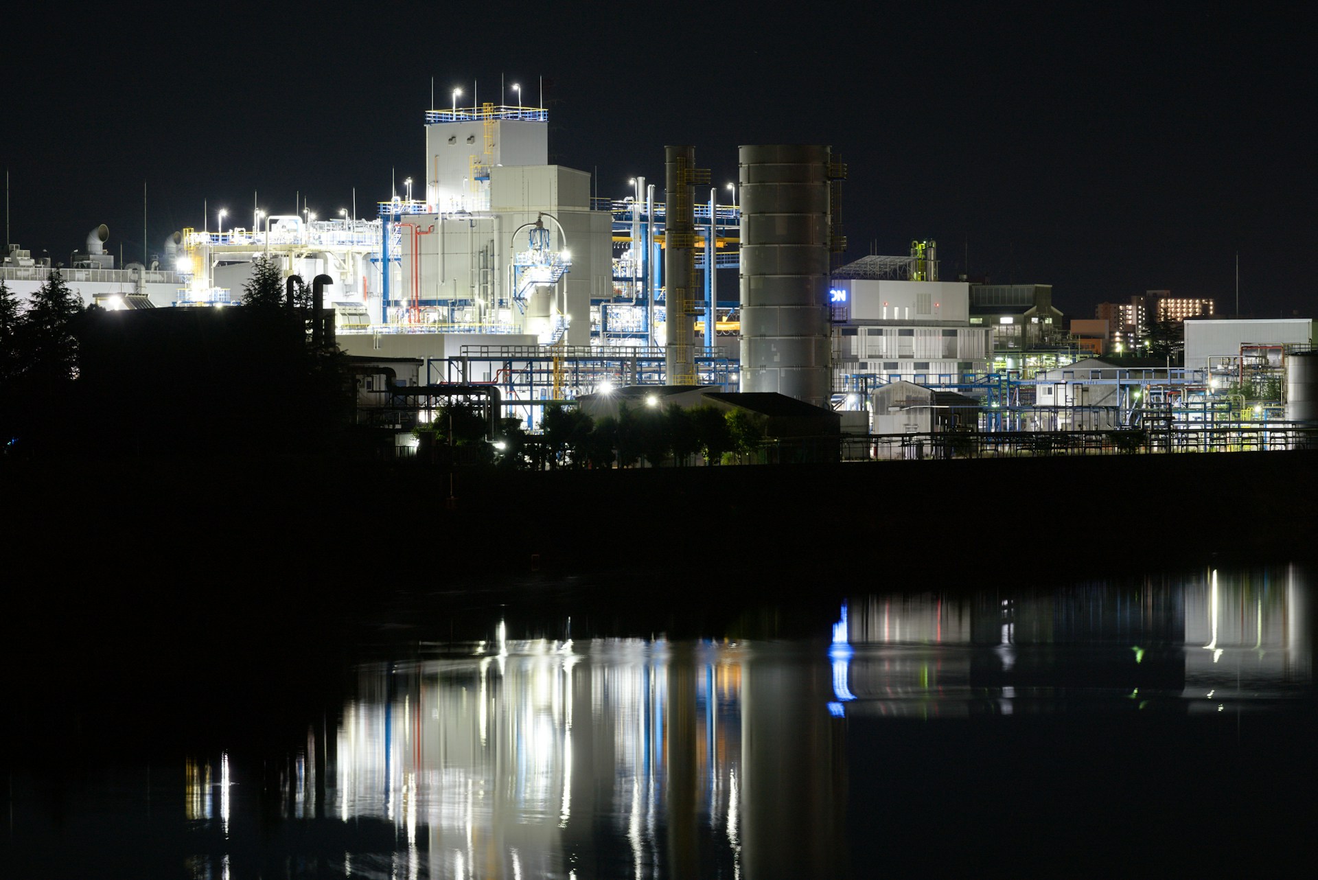 Industrial facility at night with water reflection — plant scale and economics context. Photo: waa towaw on Unsplash.